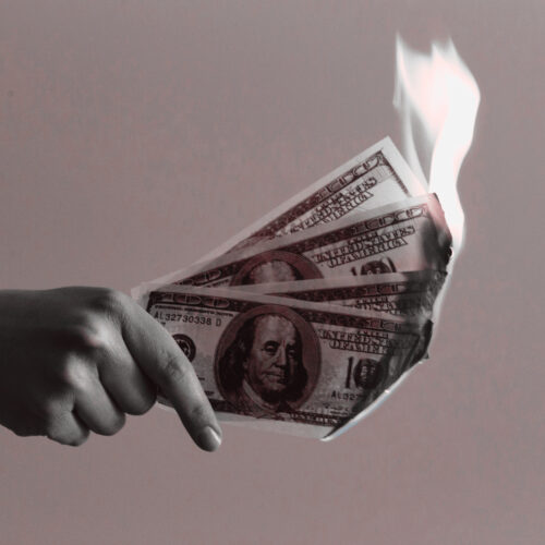 womans hand holding three flaming hundred dollar bills